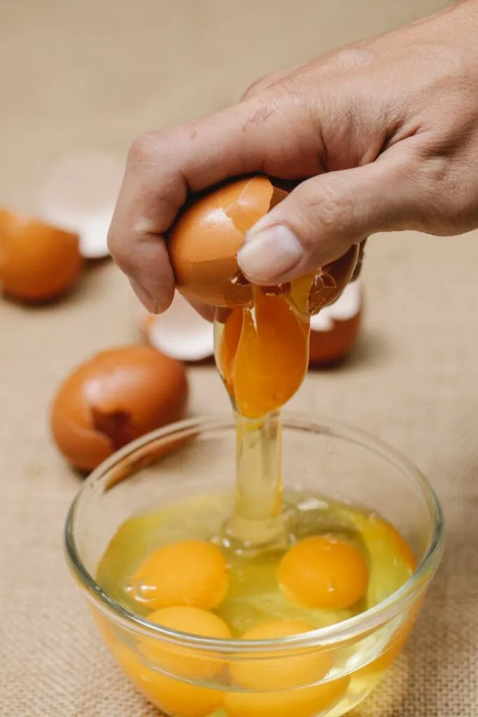Woman adding raw chicken egg in glass bowl
